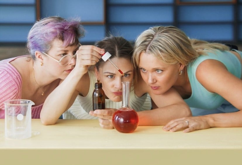 tre unge kvinner ser nøye på pipette og glasskolbe med rød væske